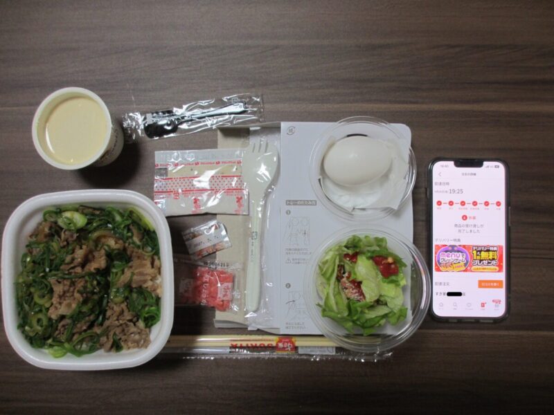 menuアプリで注文したすき家の料理と、配達完了画面が表示されたスマートフォンの様子